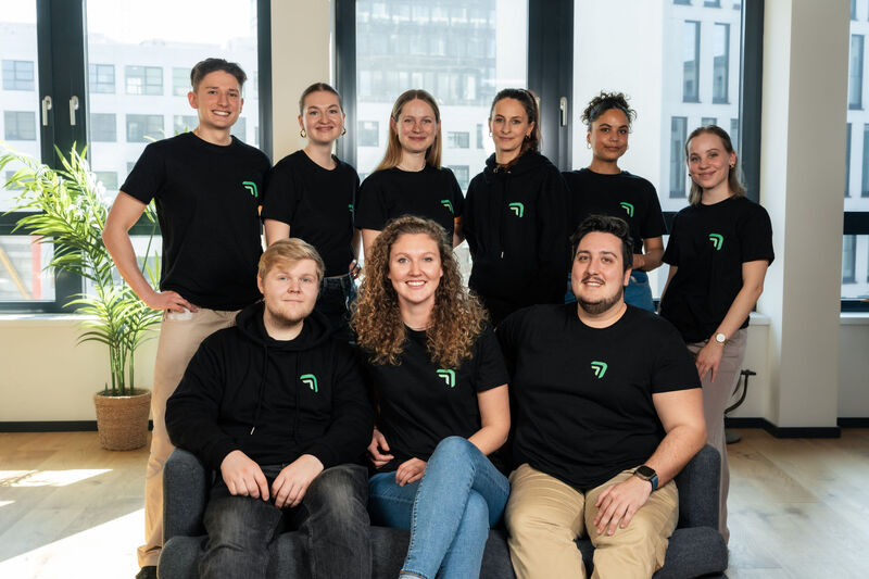 Das Sales-Team von summ.ai in einheitlichen schwarzen Shirts mit Logo in einem hellen Büro. Hinten von links nach rechts: Leo Hermanutz, Emilia Zaiser, Vanessa König, Sarah Sebesta, Laila Haas und Alexandra Eberle. Vorne sitzend von links nach rechts: Julian Novak, Flora Geske und Fabian Langer.