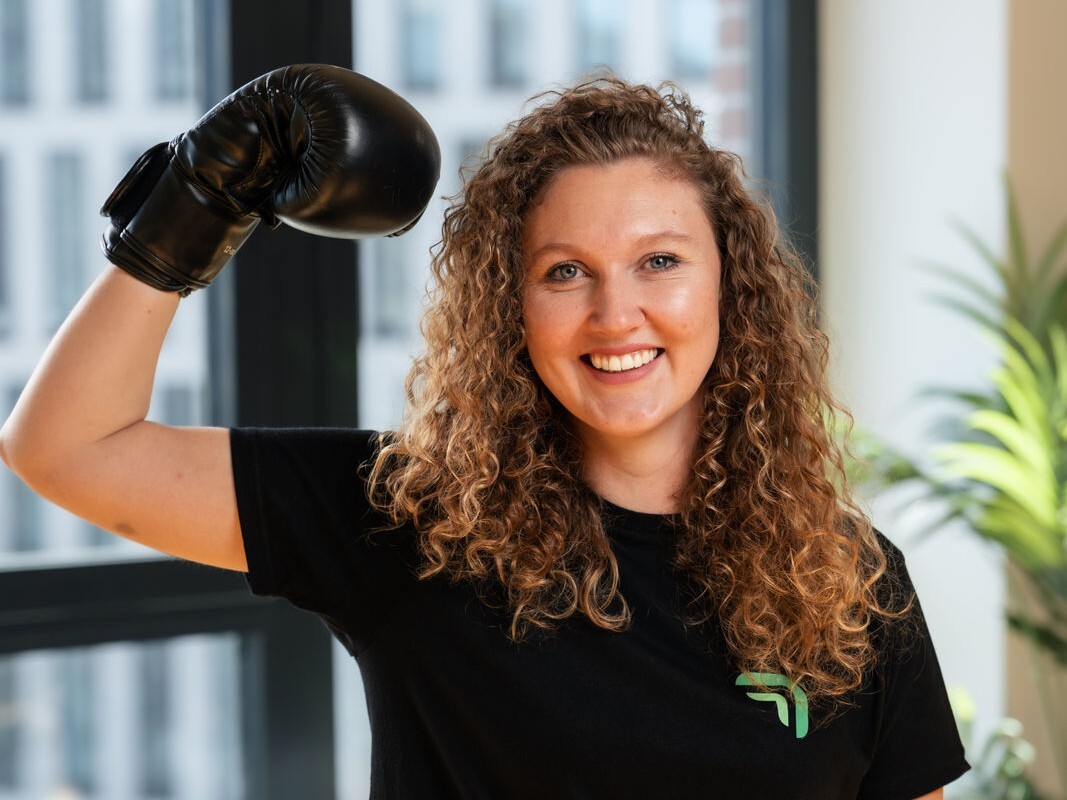 Flora Geske, CEO von summ.ai, lacht in die Kamera und hebt einen Arm mit Boxhandschuh.
