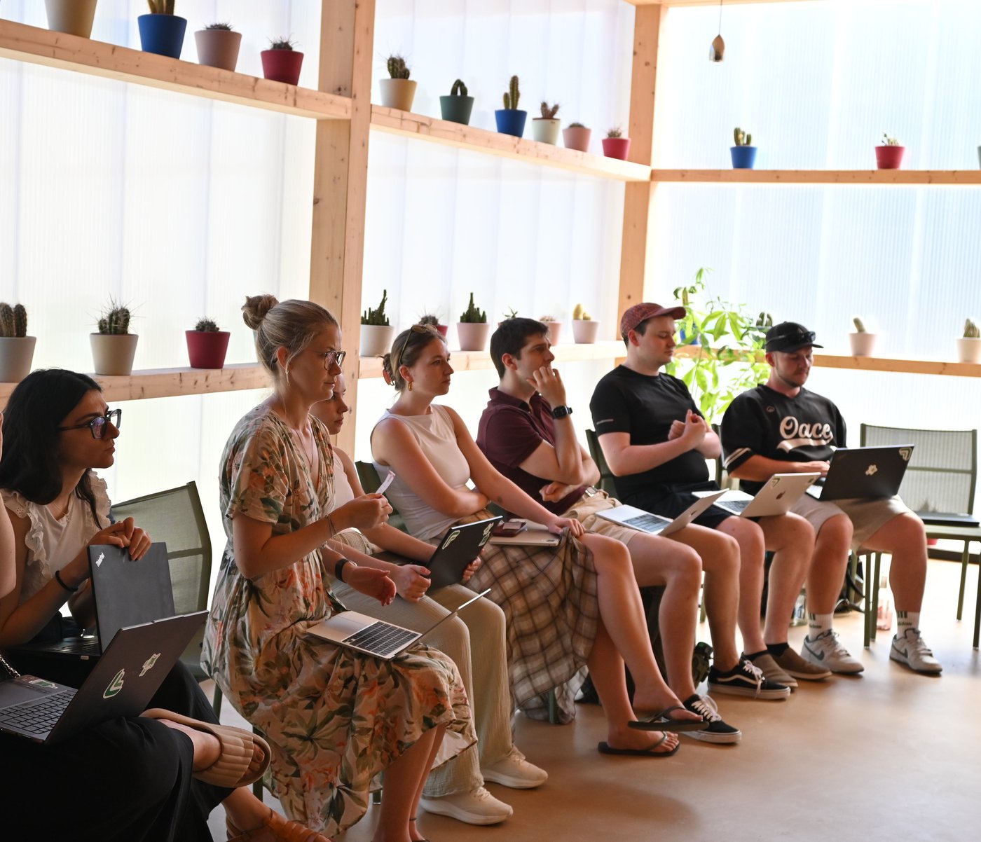Teammitglieder von summ.ai sitzen beim Offsite 2026 mit Laptops in einer Reihe und hören aufmerksam einem Vortrag zu, im Hintergrund Regale mit Kakteen.