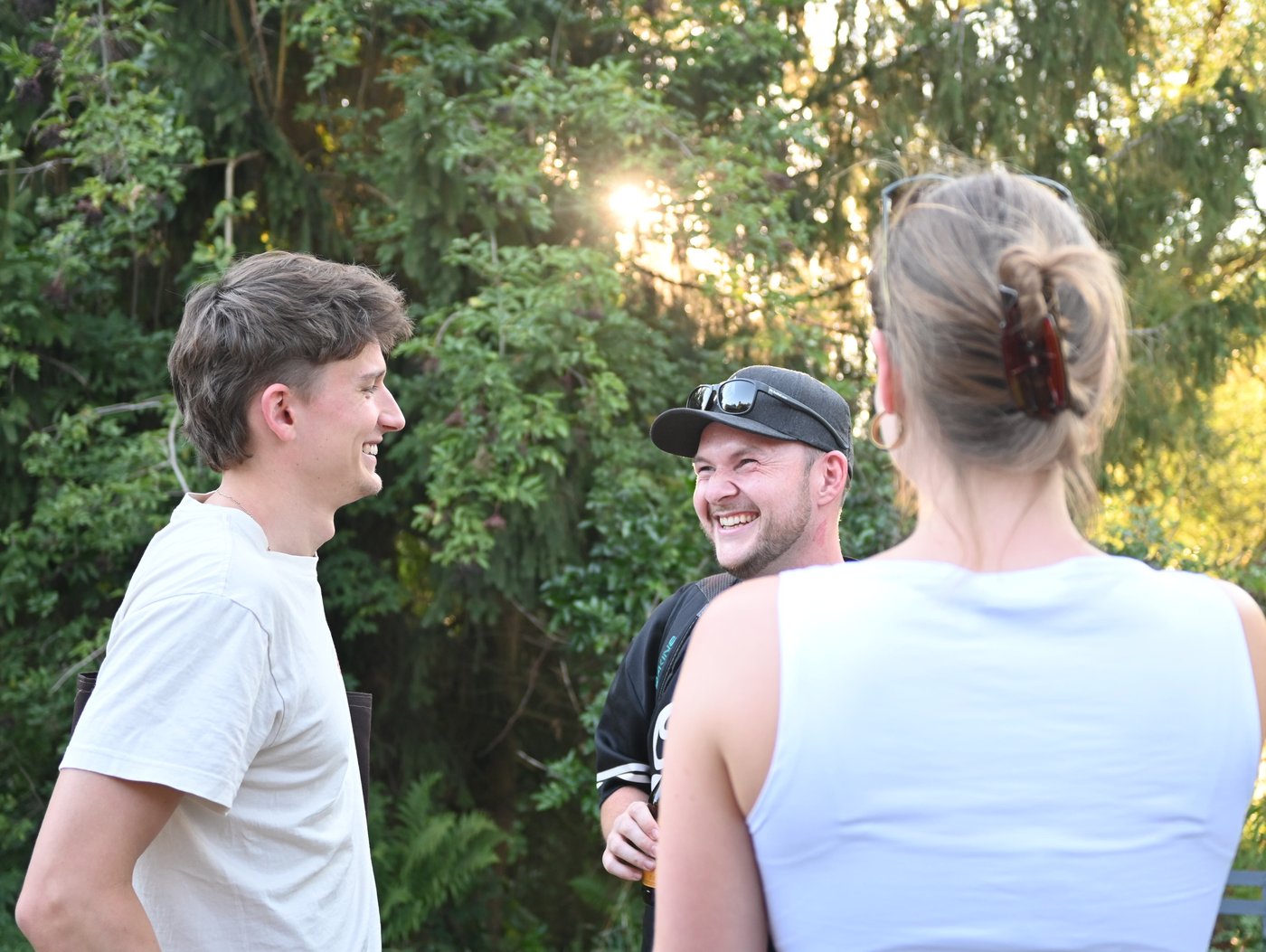 Drei Teammitglieder von summ.ai unterhalten sich beim Offsite 2026 lachend im Freien vor grünen Bäumen in der Abendsonne.