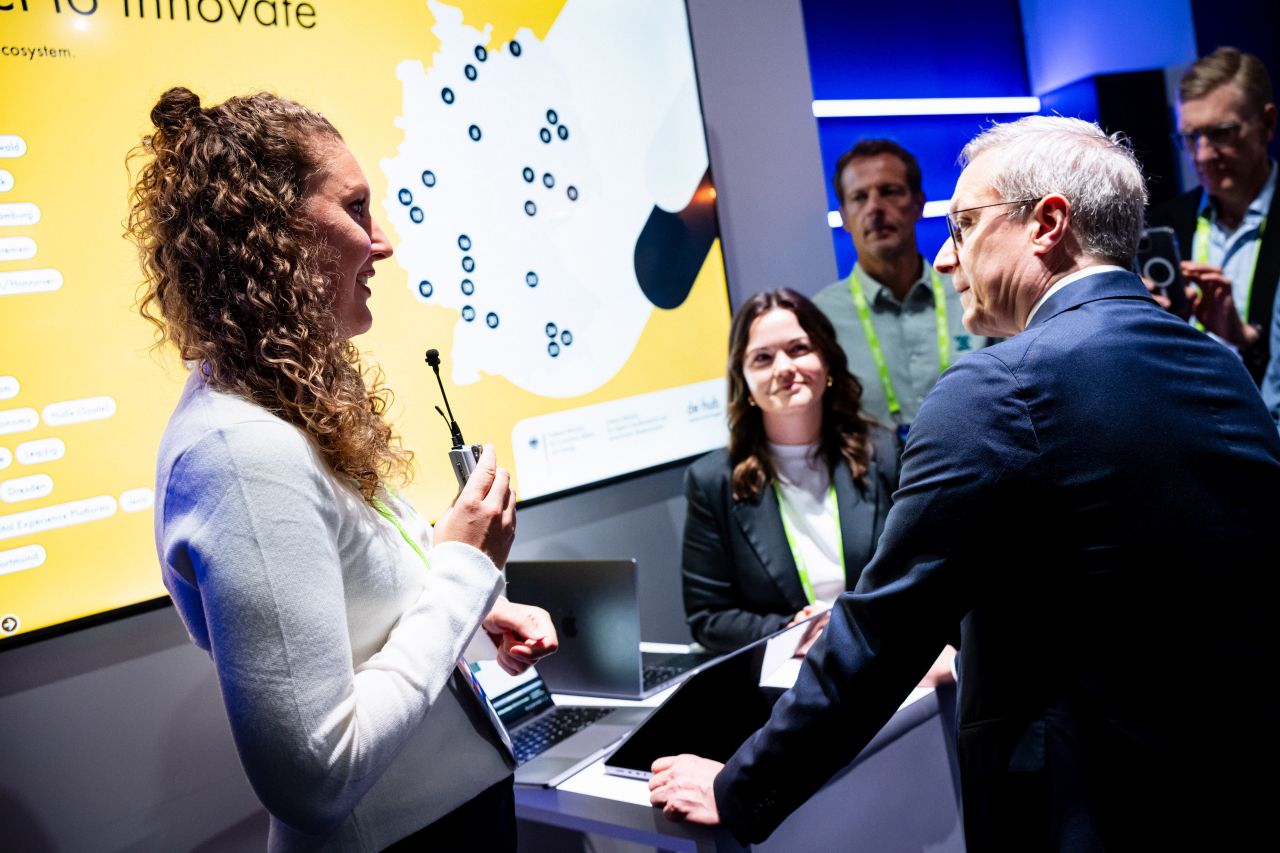 Flora Geske, CEO von summ.ai, stellt Bundesdigitalminister Karsten Wildberger an einem Stand ihre Software vor. Im Hintergrund eine Karte der de:hub Standorte in Deutschland und weitere Besucher.