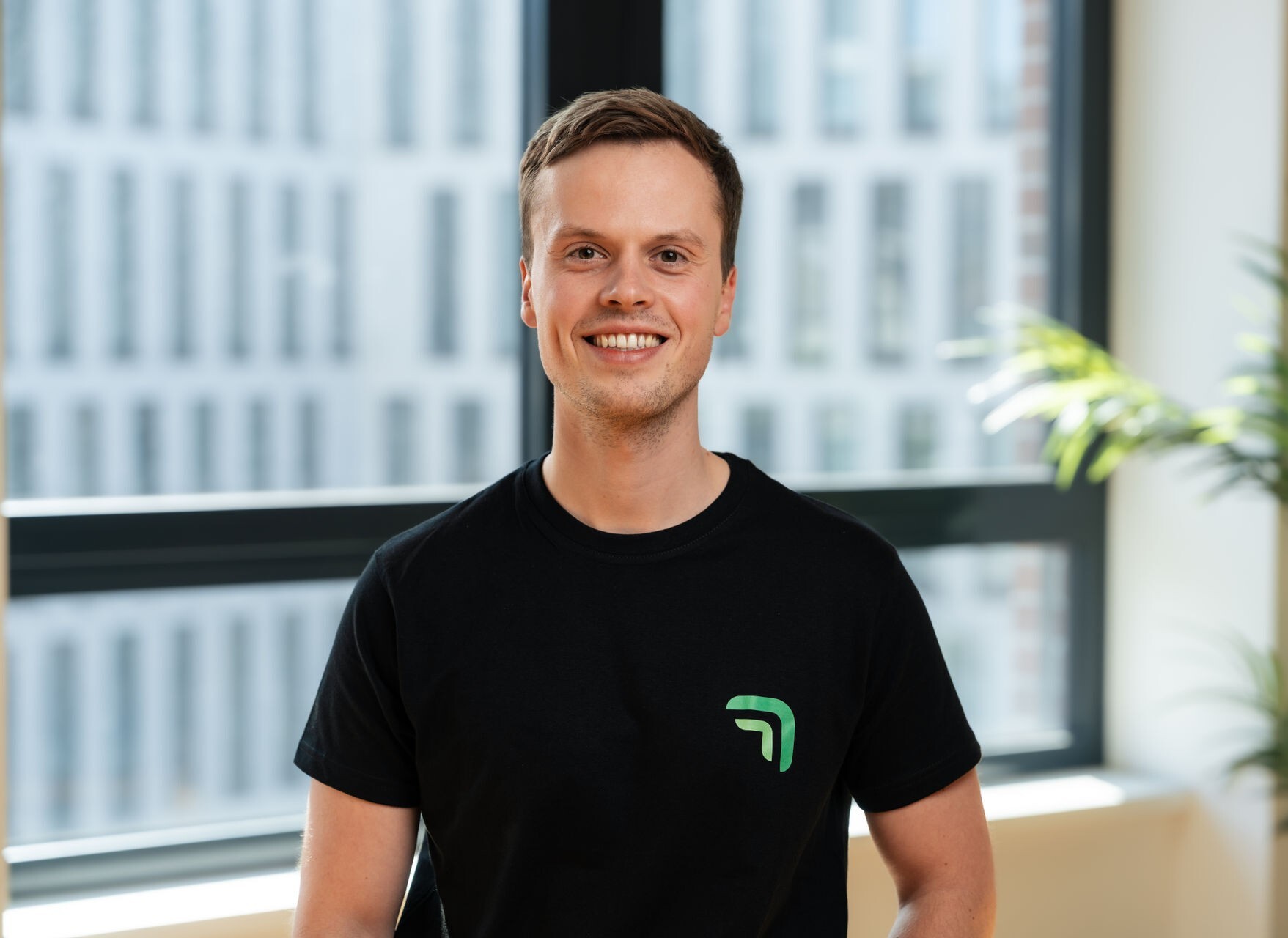 Nicholas Wolf, Gründer und CTO von summ.ai, lächelt in die Kamera vor einem großen Bürofenster.
