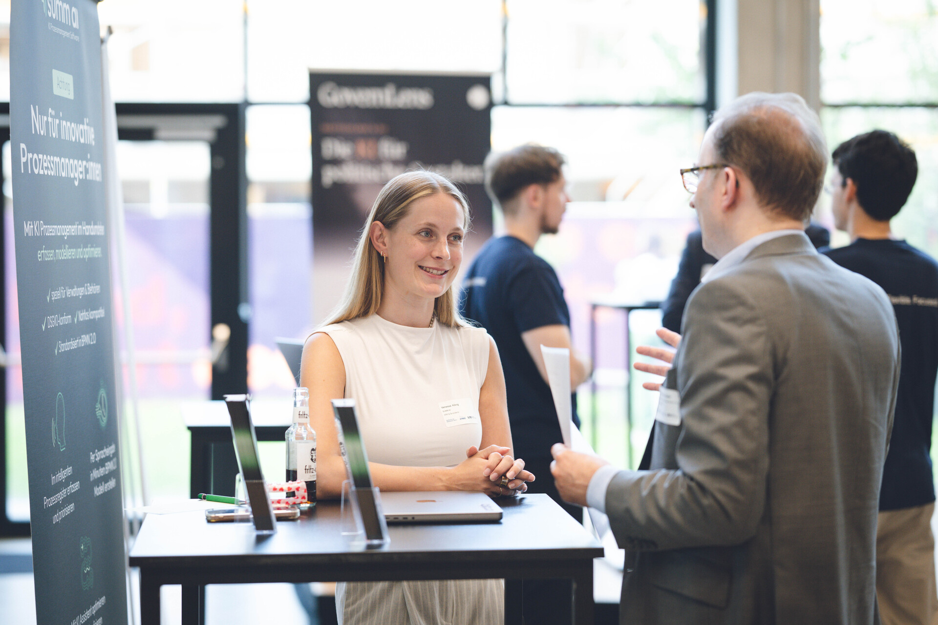 anessa König, CRO von summ.ai, steht lächelnd an einem Stehtisch am summ.ai Messestand und spricht mit eine