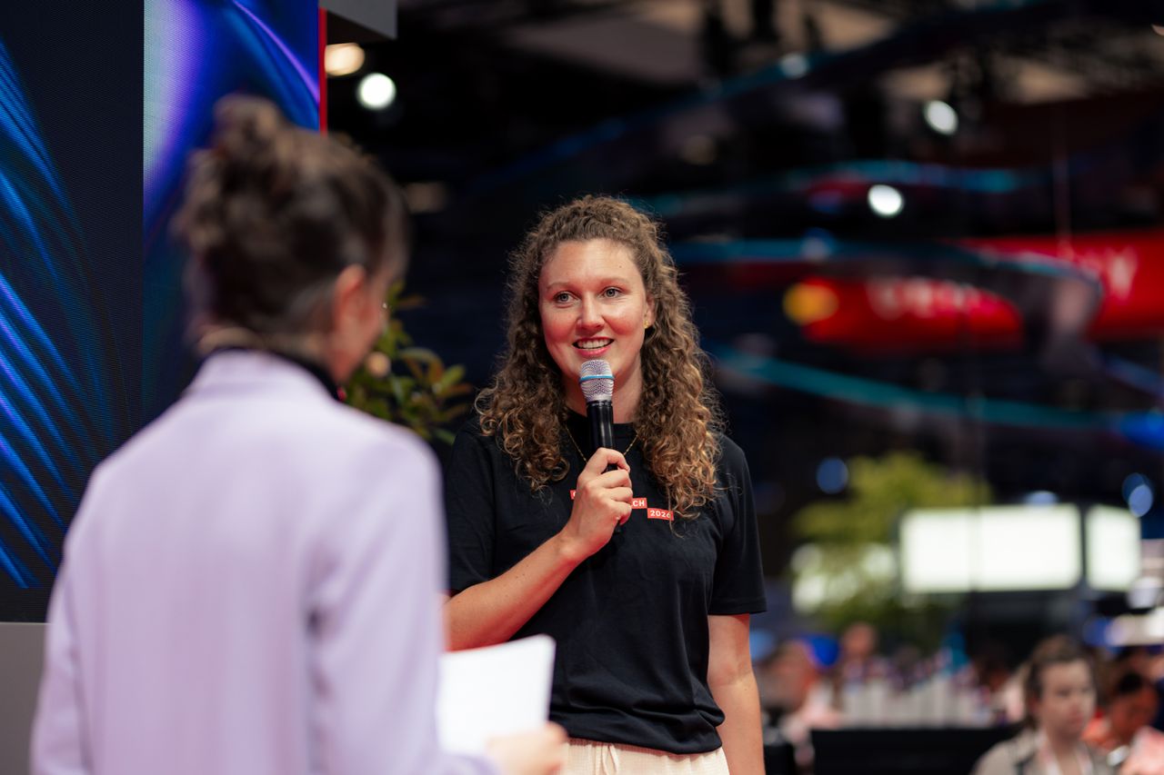 Flora Geske, CEO von summ.ai, steht mit Mikrofon auf einer Bühne der VivaTech 2026 in Paris und spricht lächelnd mit einer Moderatorin, im Hintergrund die große Veranstaltungshalle.